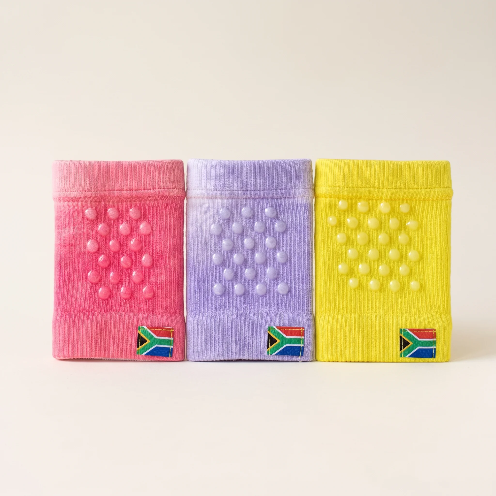 All three knee protector colourways lined up together: sunshine yellow, lavender and pink, back panel up, showing the grip dots side by side